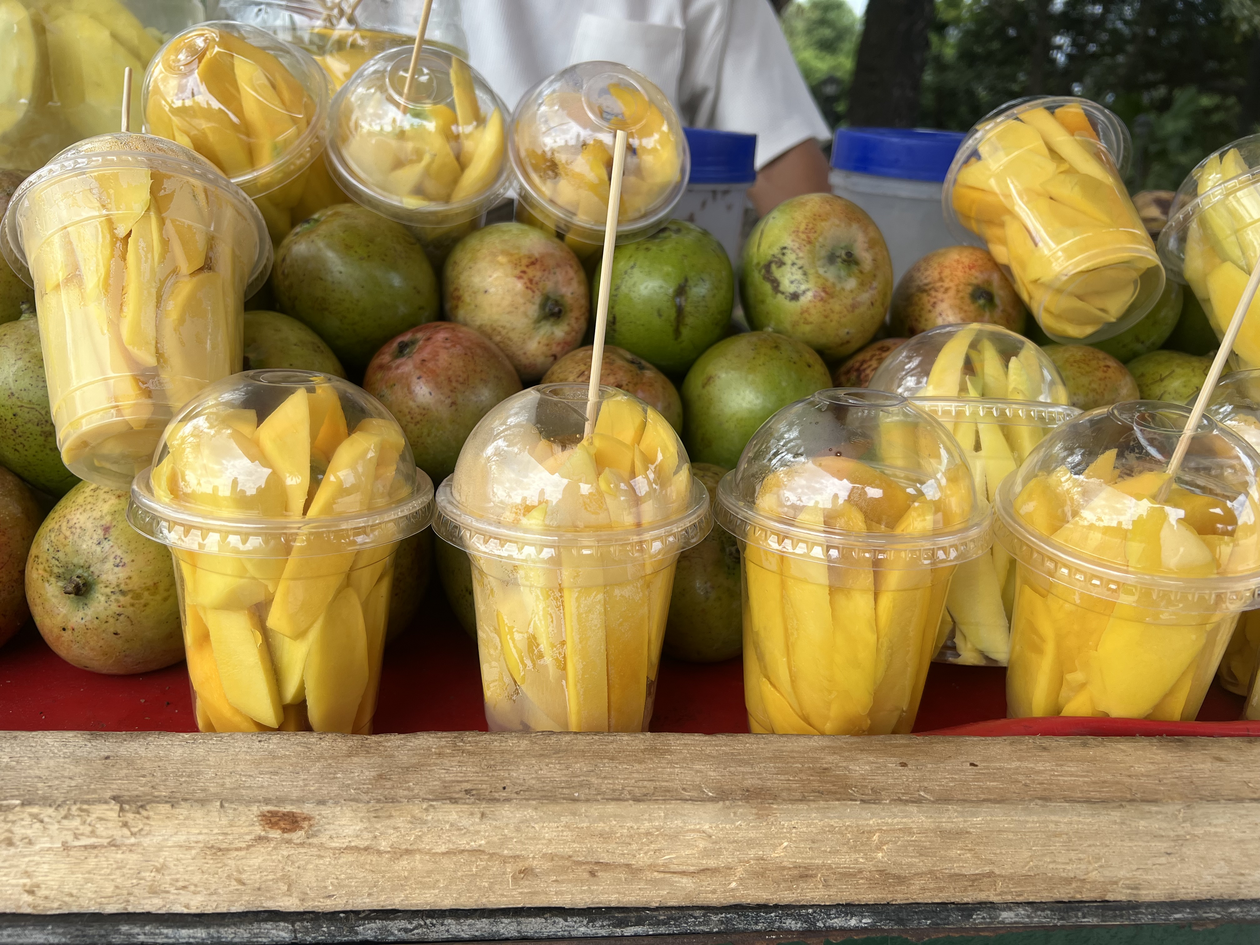 A street vendor's stall is filled with fresh mangoes and plastic cups of sliced mangoes ready to eat.