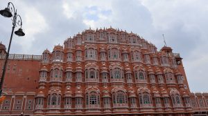 A close-up view of Jaipur&rsquo;s iconic Hawa Mahal, showcasing its intricate latticework, ornate windows, and delicate domes, all set dramatically against a cloudy sky.