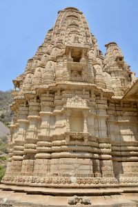 An intricately carved stone temple tower in Bhangarh Fort, Alwar, Rajasthan, displays stunning ancient architecture against a clear blue sky.