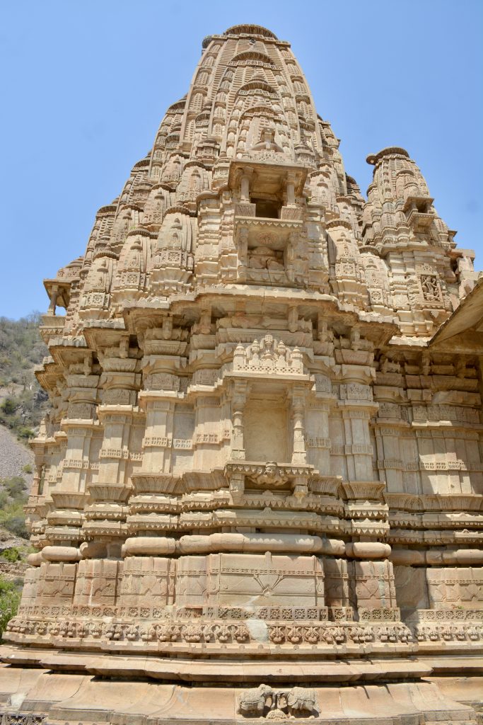 An intricately carved stone temple tower in Bhangarh Fort, Alwar, Rajasthan, displays stunning ancient architecture against a clear blue sky.