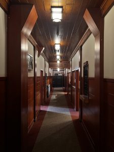 Narrow hallway of a vintage lodge, centered with door open to each site, wooden panel walls and a sign for a giftshop atop one of the doorways
