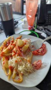 A close-up view of a fork holding a bite-sized portion of food, featuring a mix of potato fries, chopped cabbage, and tomato slices topped with ketchup.