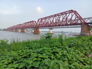 A picture of a red coloured bridge which is supported by big cemented stands in between, underneath is a river. Bhairab, Kishoreganj, Bangladesh 