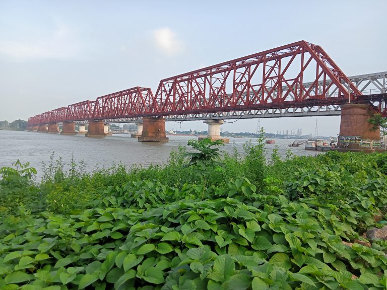 A picture of a red coloured bridge which is supported by big cemented stands in between, underneath is a river. Bhairab, Kishoreganj, Bangladesh