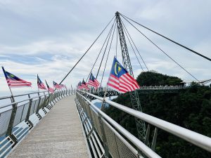 Malaysian flags line the railing of the SkyBridge, a curved pedestrian bridge above a green forest, in Langkawi, Malaysia.