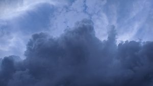 A dramatic sky filled with dark, billowing clouds dominating the image, set against a lighter blue backdrop.
