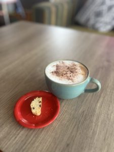 A cappuccino in a light blue mug with a small cookie on a red saucer #SummerPhotoContest
