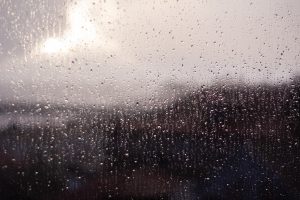 A close-up view of a window covered in raindrops, with a soft focus. 