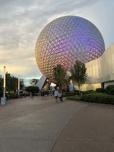 People exiting Epcot Disney in Orlando, FL, as the sun is setting, catching different color spectrums off the dome. 
