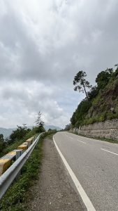A winding road with yellow-black guardrails curves through the hills of Himanchal.