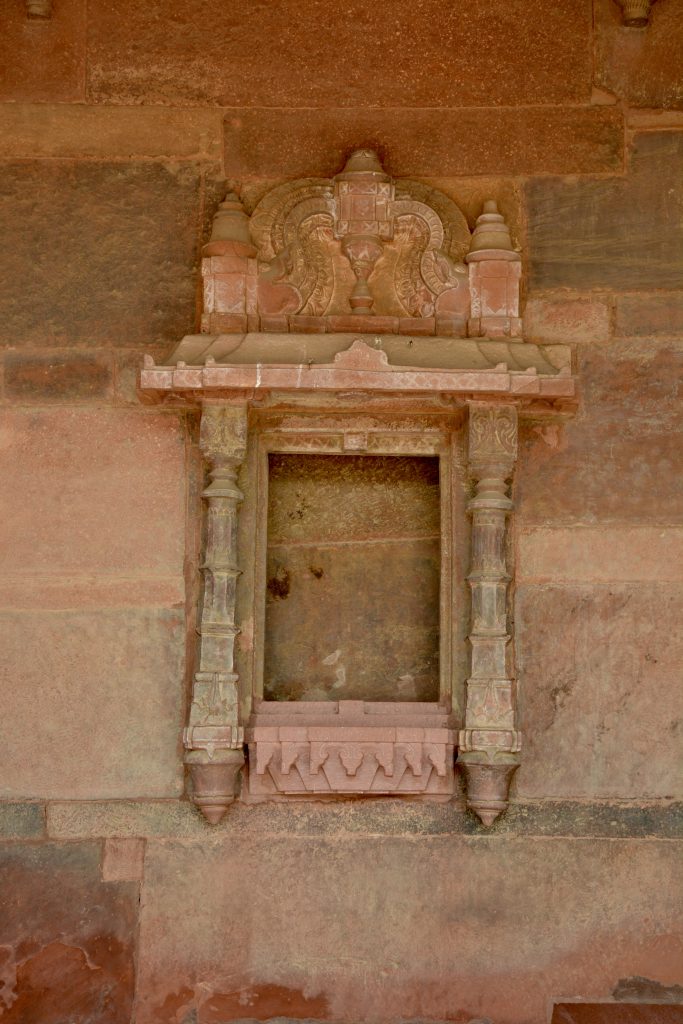 An ornate red sandstone niche with intricate carvings, showcasing Mughal architectural detail. Captured at Fatehpur Sikri, Uttar Pradesh.