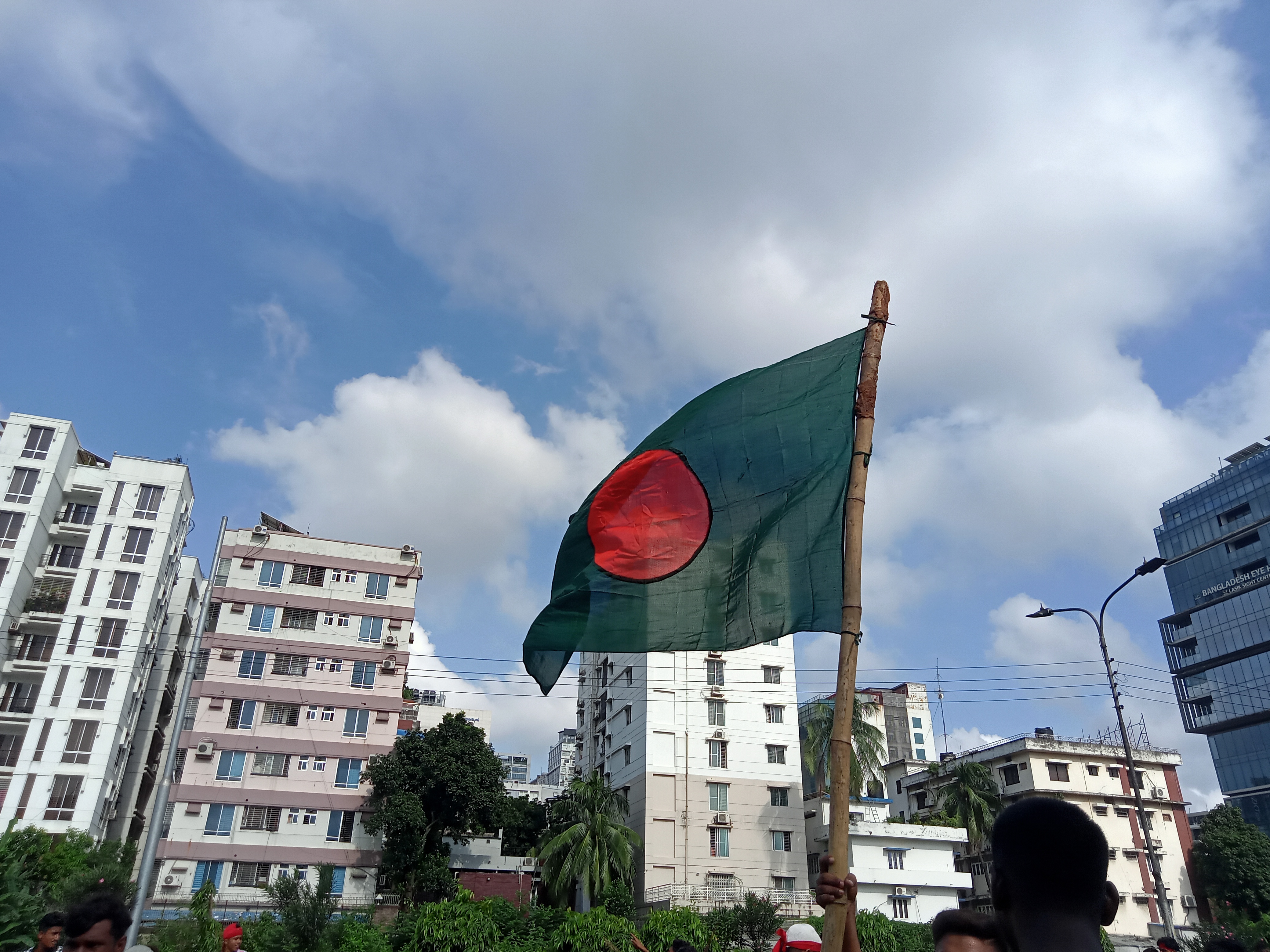 36th July, July Movement of Bangladesh. A person is holding a flag of Bangladesh made of green fabric with a red circle at its center.