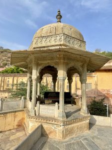 An intricately carved stone pavilion with a domed roof at Amer Fort, Jaipur, glows under the afternoon sun.