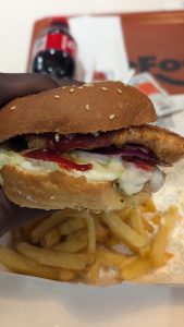 A mouth watering chicken burger held by an African hand with blurred fries in the background