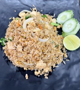 A plate of chicken fried rice with sliced onions, carrots, and a side of cucumber slices and a lime wedge.

