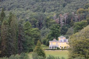 Dochfour Estate House, painted a soft primrose yellow with classic Georgian windows, is surrounded by a variety of trees.