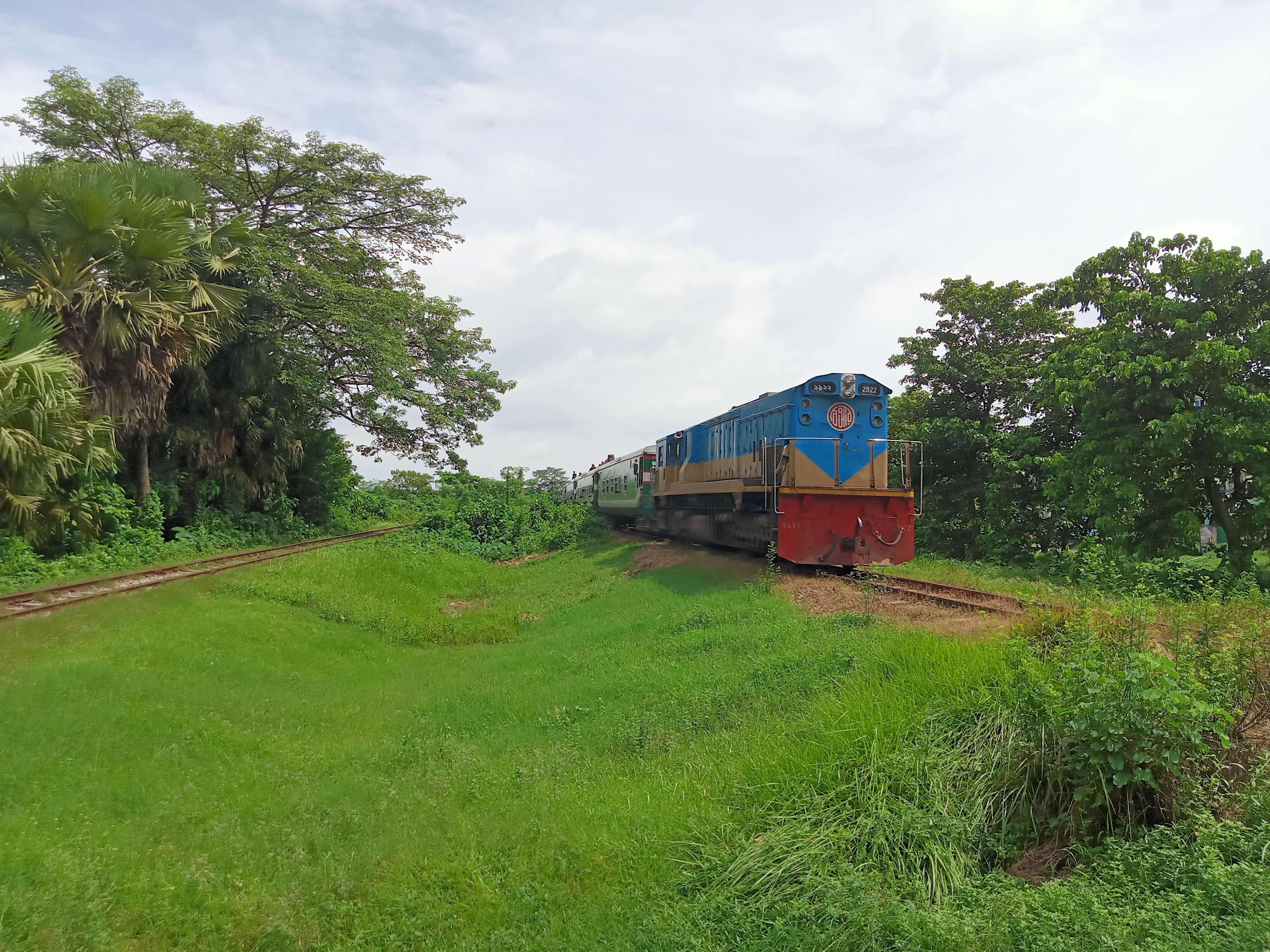 A diesel locomotive is navigating a curve on a railway line surrounded by lush green grass and trees.