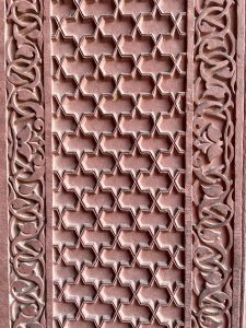 Close-up of an intricate sandstone lattice pattern, finely carved with geometric and floral designs. Captured at Fatehpur Sikri, Uttar Pradesh.