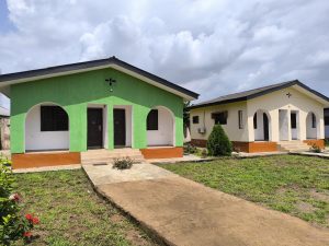 Two modern buildings are depicted in the image. The building on the left is painted green with arched windows and doors, while the one on the right is painted yellow with a similar arched design