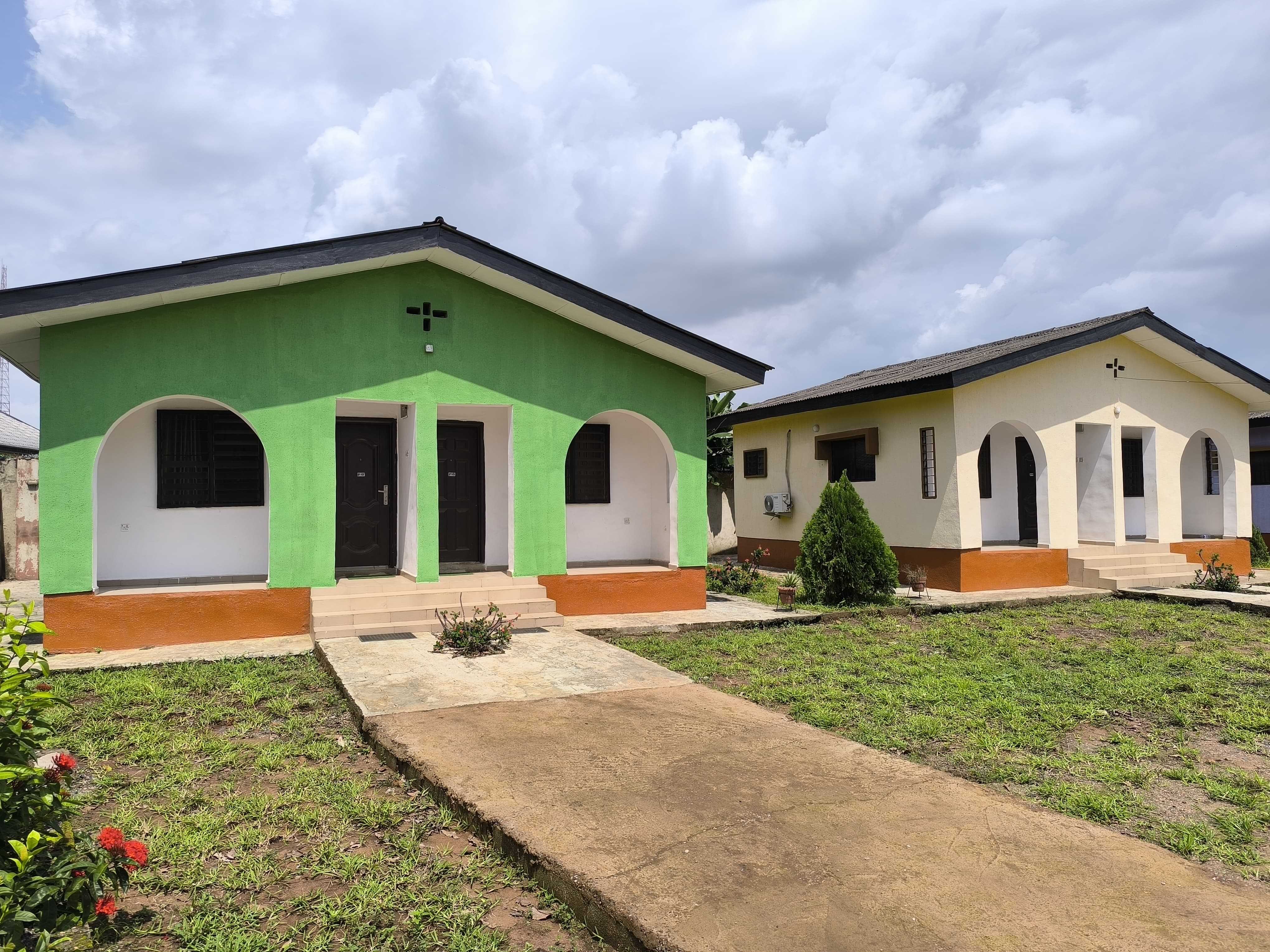 Two modern buildings are depicted in the image. The building on the left is painted green with arched windows and doors, while the one on the right is painted yellow with a similar arched design