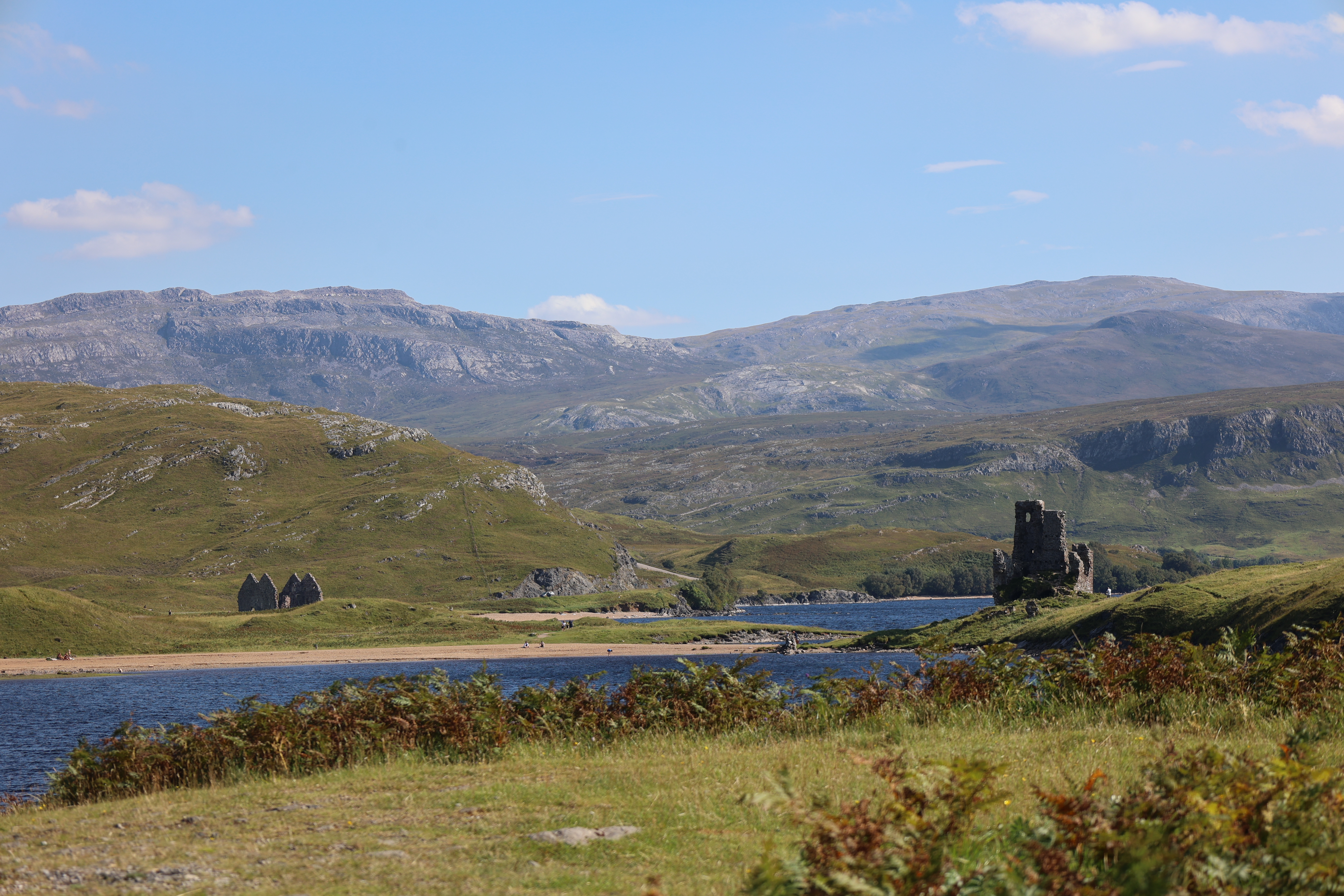 

Ardvreck Castle ruins in the Scottish Highlands, with a sandy beach, shimmering loch, and towering hills.