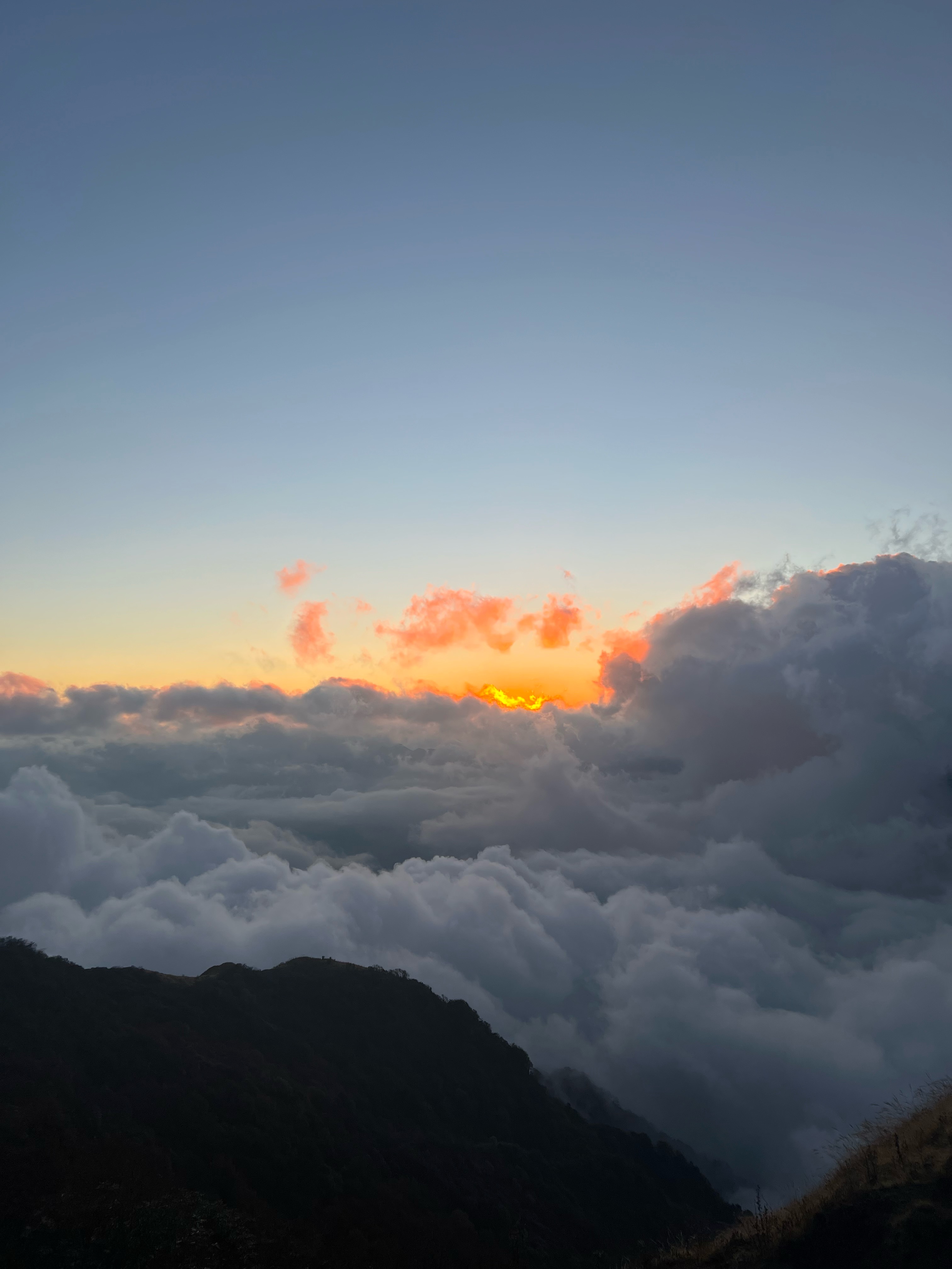 A view from a high altitude of a sky with layered clouds, a sliver of golden light visible between them as the sun sets.