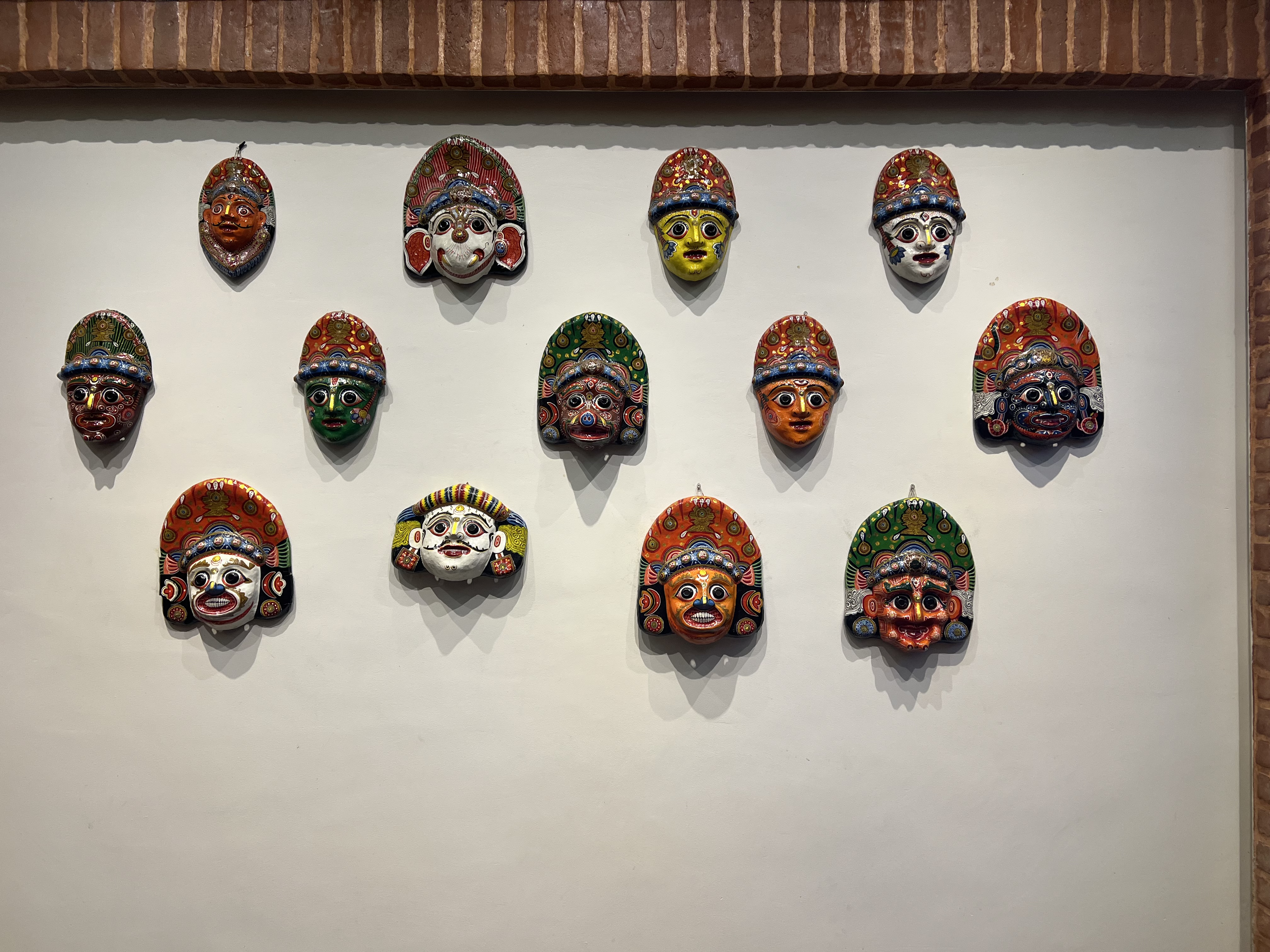 A collection of colorful traditional Newari masks, arranged on a white wall.