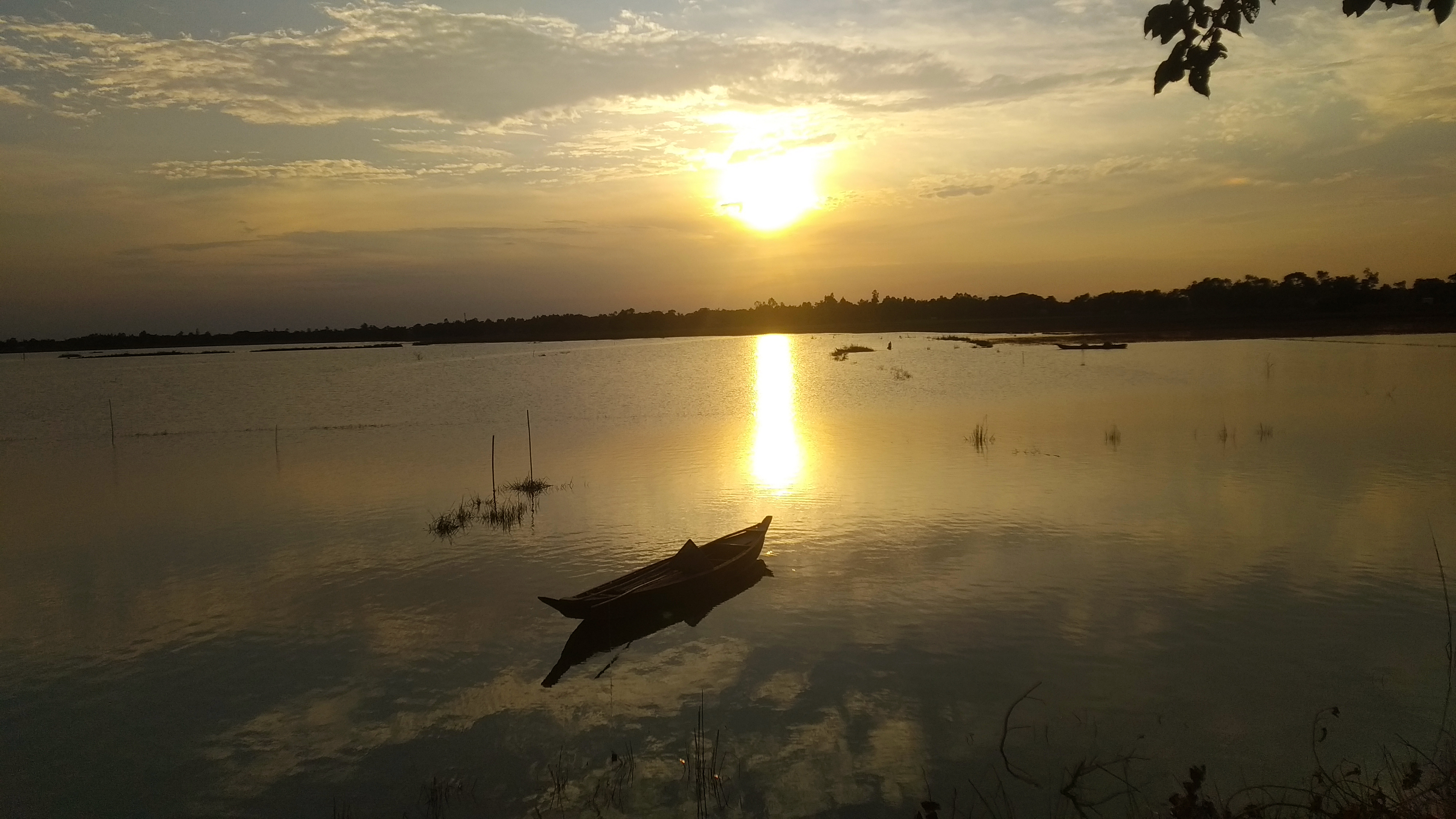 A serene sunset over a calm body of water, with the sun casting a golden reflection on the surface.