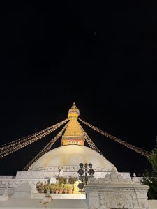 A nighttime view of a large stupa adorned with colorful prayer flags. 