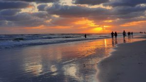 A scenic Florida beach at sunset, featuring vibrant orange and purple hues in the sky with fluffy clouds.
