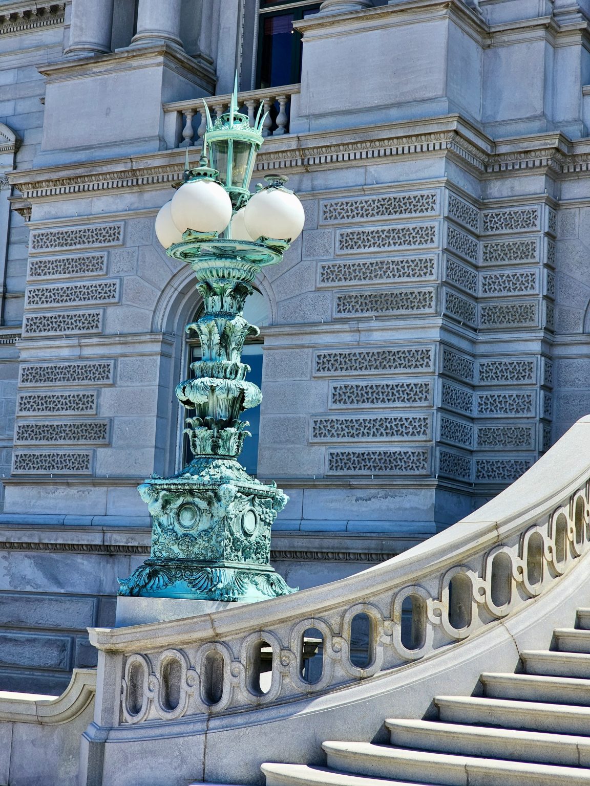 An antique bronze lamp post with intricate detailing stands beside the grand stone steps of a historic building in Washington, D.C., United States.