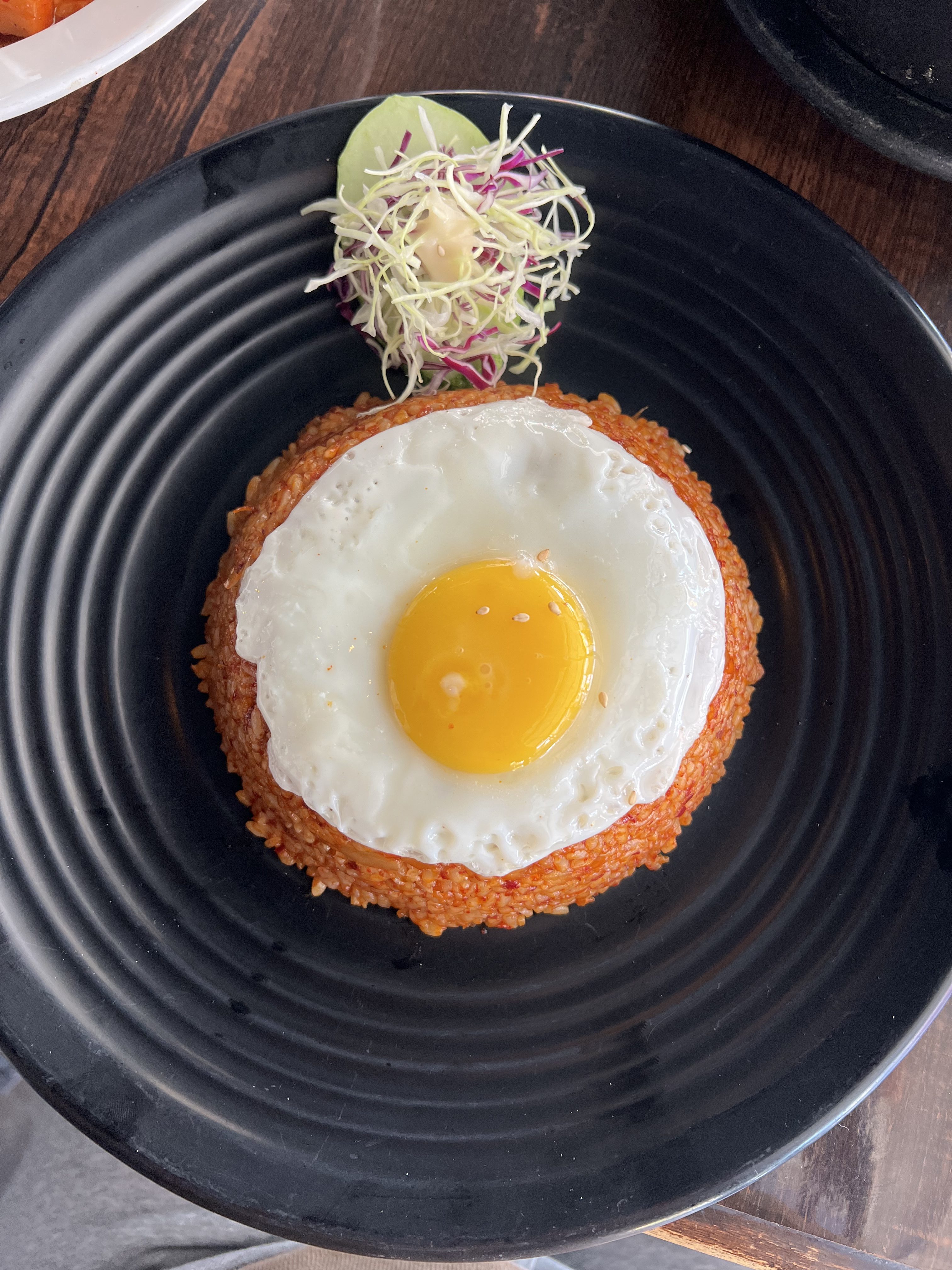 A plate of kimchi fried rice topped with a sunny-side-up fried egg and a small side salad.