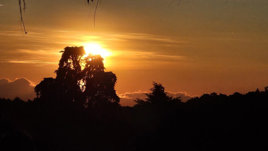 A sunset scene with the sun glowing brightly on the horizon, casting warm orange and yellow hues across the sky.
