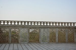 A marble railing adorned with traditional jali designs, offering a view of lush greenery beyond. Captured at Agra Fort, Uttar Pradesh, India. 