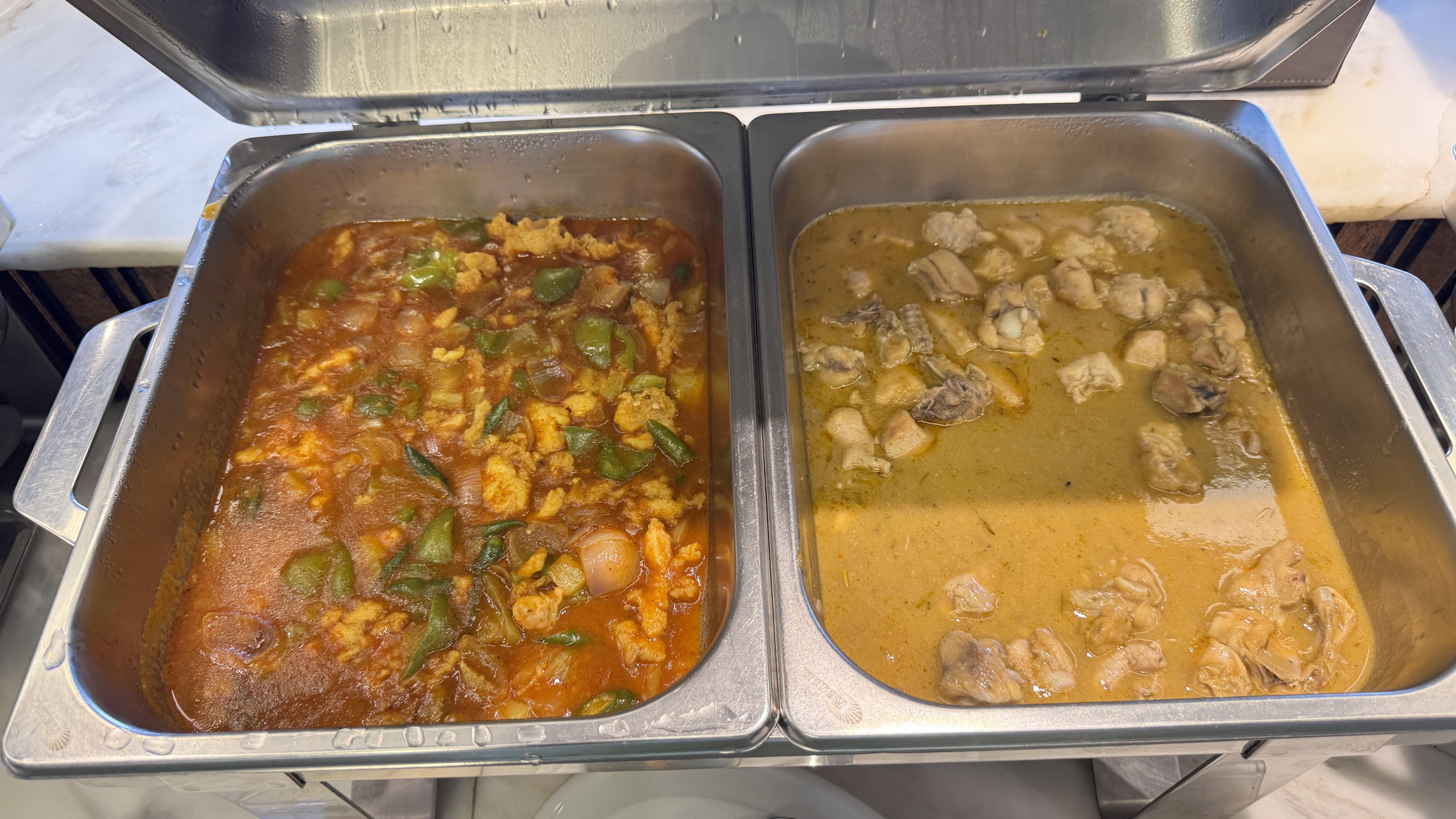 A side-by-side buffet with spicy red chicken chili on the left and milder yellow chicken curry on the right.