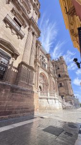 
A photo featuring a majestic historical building with intricate architectural details, including tall columns and ornate facades, set along the charming streets of M&aacute;laga.