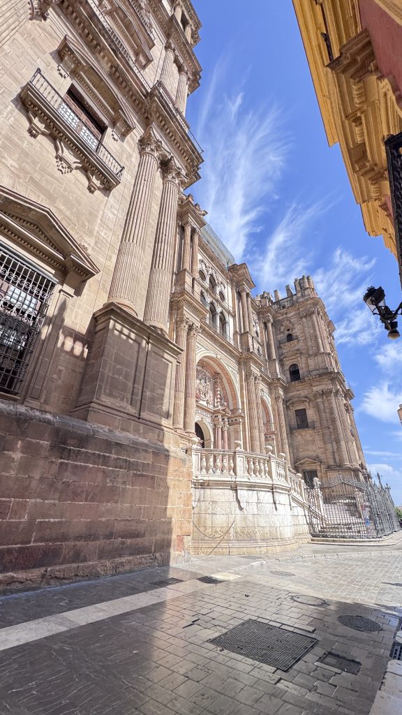 A photo featuring a majestic historical building with intricate architectural details, including tall columns and ornate facades, set along the charming streets of Málaga.