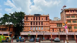 Bairathi Bhawan, an old building in Jaipur’s Johri Bazar walled city, showcasing historic architecture. Cars are parked infront of the building. Auto and Rickshaw are also in the road.
