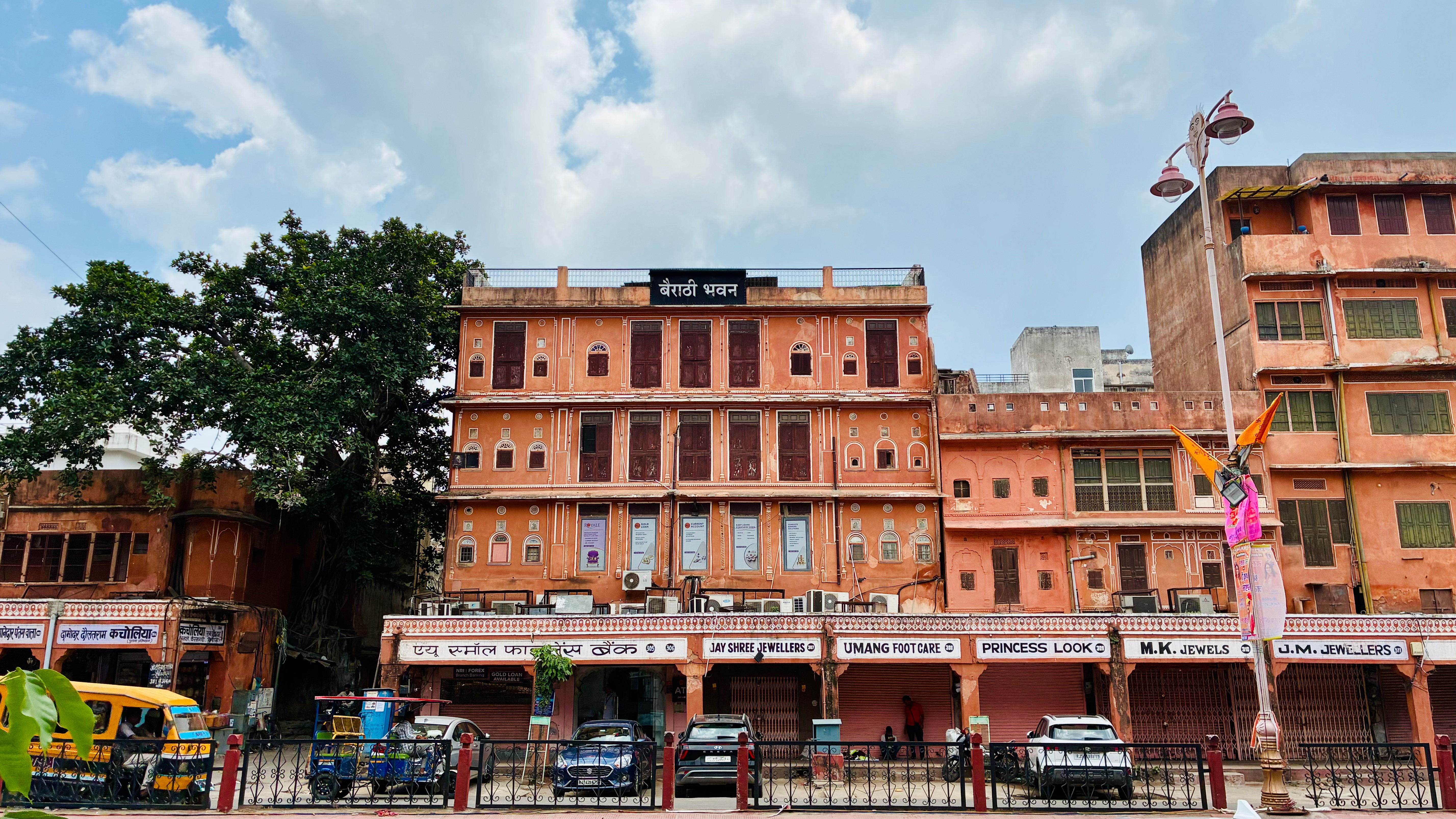 Bairathi Bhawan, an old building in Jaipur's Johri Bazar walled city, showcasing historic architecture. Cars are parked infront of the building. Auto and Rickshaw are also in the road.