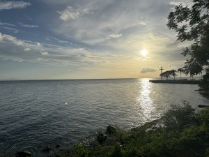 A tranquil coastal scene during sunset, with the sun low in the sky casting a warm glow over the water.
