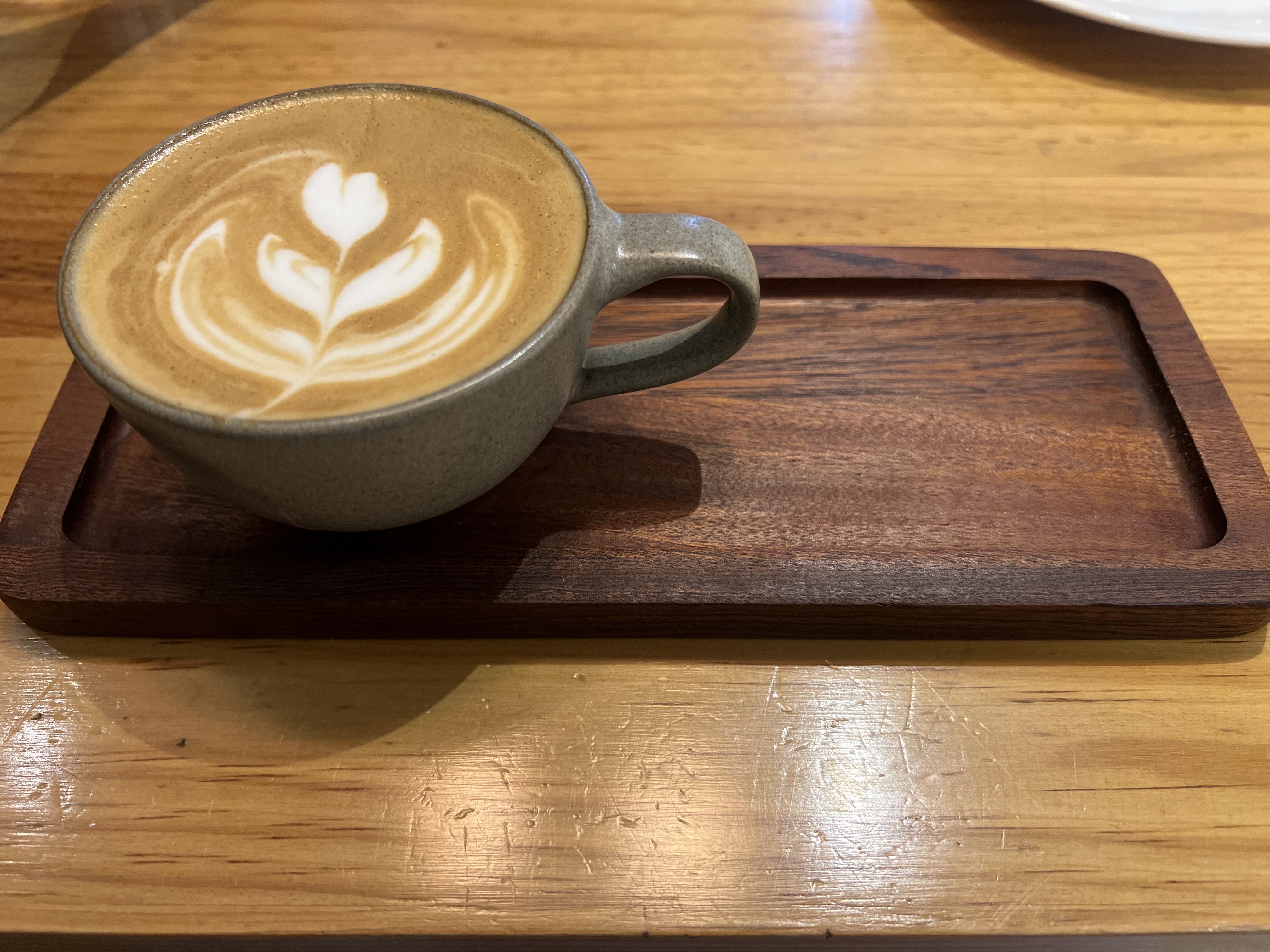 A cup of latte with a heart-shaped design in the foam sits on a wooden tray on a wooden table.

