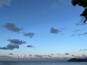 A sceneric seascape view with a large sky portion and full of scattered clouds and a small portion of a distant mountain.