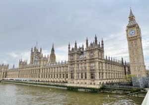 The Houses of Parliament and Big Ben in London, as seen from across the River Thames on a cloudy day.