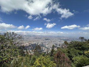 A picture taken from a top of a beautiful crowded city with tall buldings surrounded by trees and jungles under the scattered cloudy sky. Bogotá desde Cerro Monserrate, Colombia #SummerPhotoContest