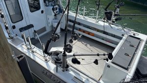 The deck of a small fishing boat, intended for just a few people.  There are fishing poles in stands  all around the edges of the boat.  You can see a little water on the far side.