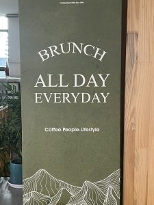 A green sign with white text that reads &quot;Brunch All Day Everyday&quot; and &quot;Coffee.People.Lifestyle.&quot;