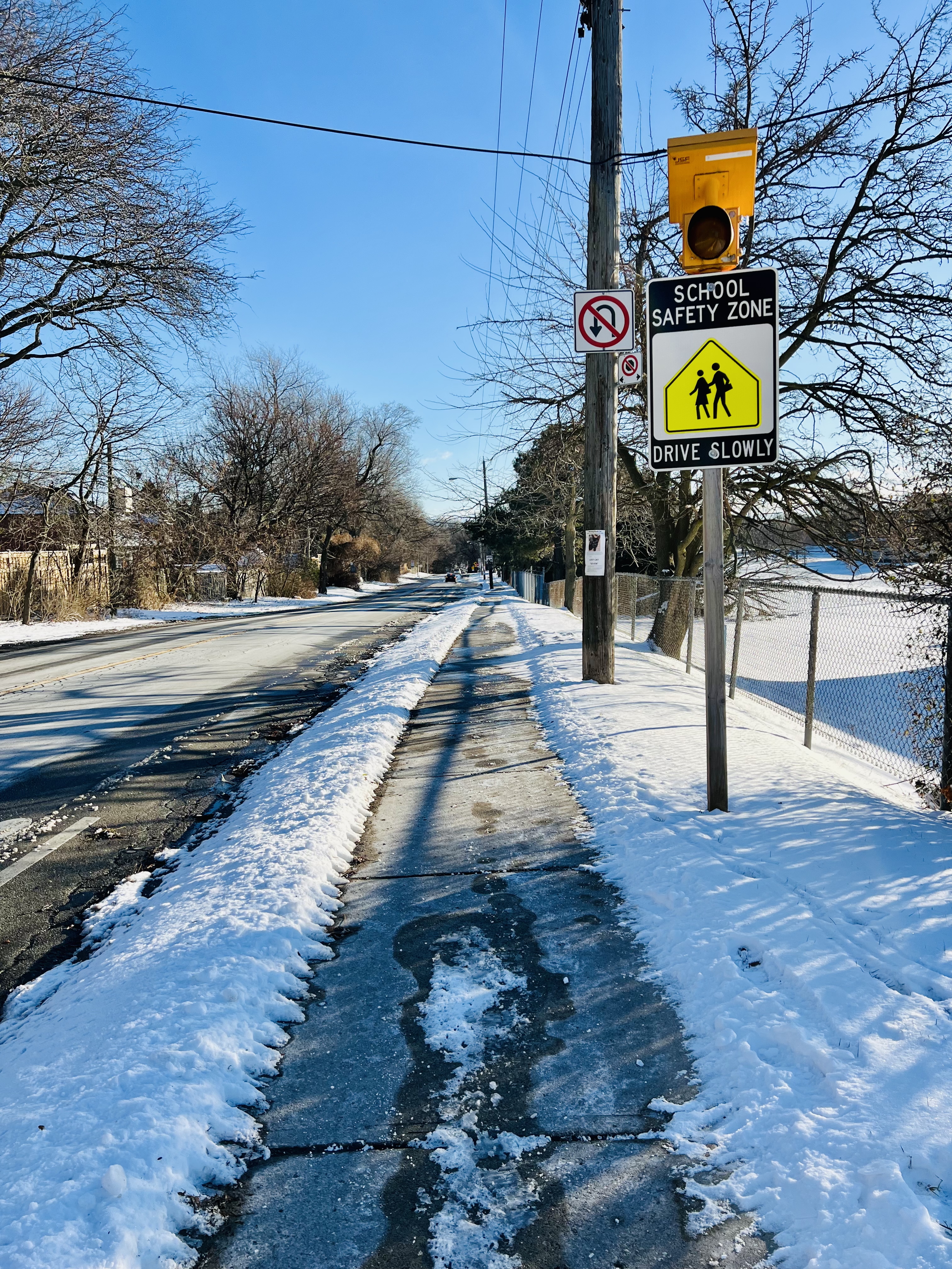 A snow-covered sidewalk next to a road with a school safety zone sign.