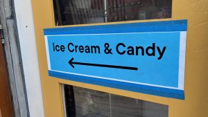 A sign taped to a door.  The sign says "Ice Cream &amp; Candy" and there's an arrow pointing to the left.