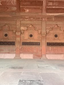 Intricately carved red sandstone jali panels with floral motifs and geometric designs, showcasing Mughal artistry inside Fatehpur Sikri, Uttar Pradesh.