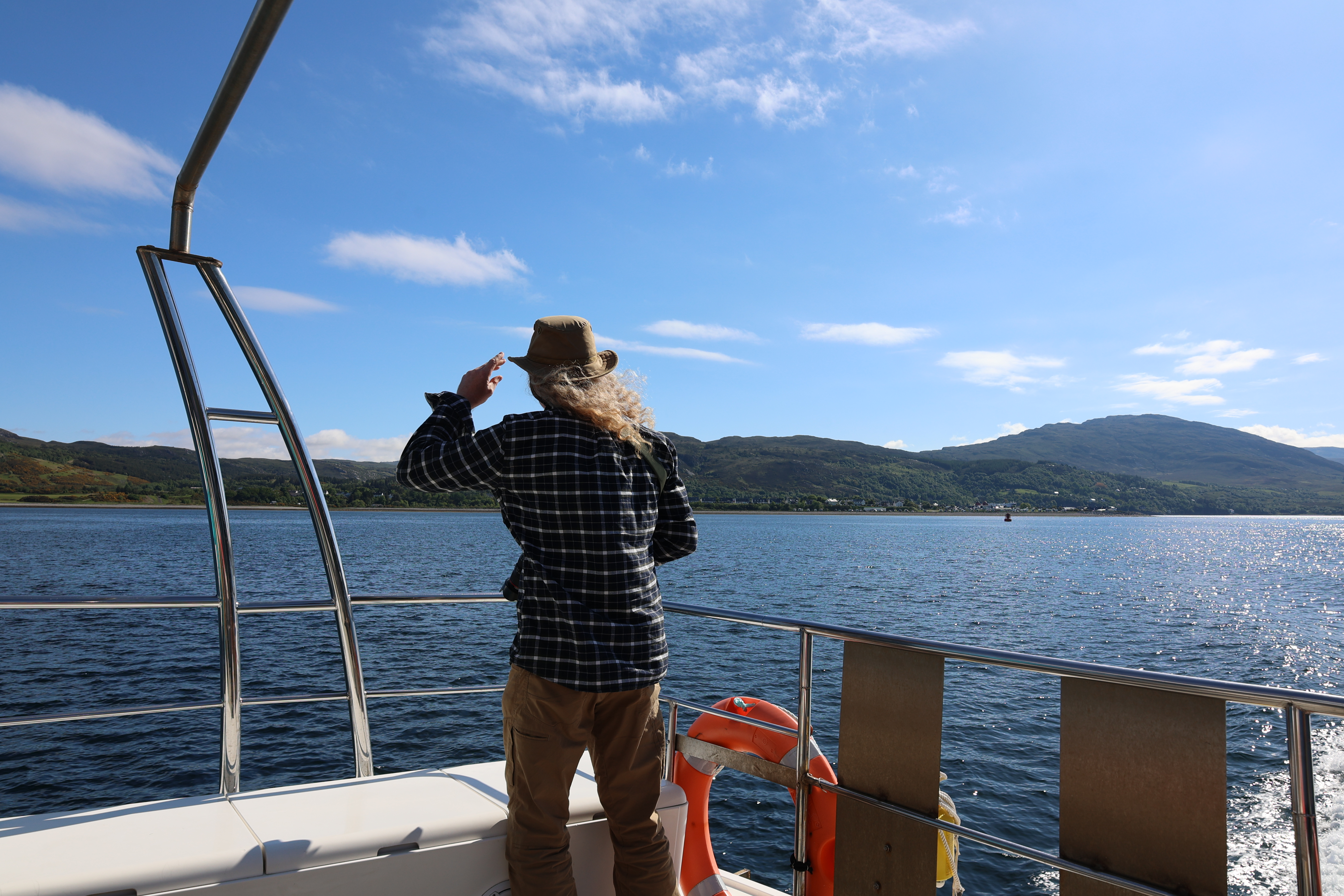 Man in a hat looking out to sea from the back of a boat